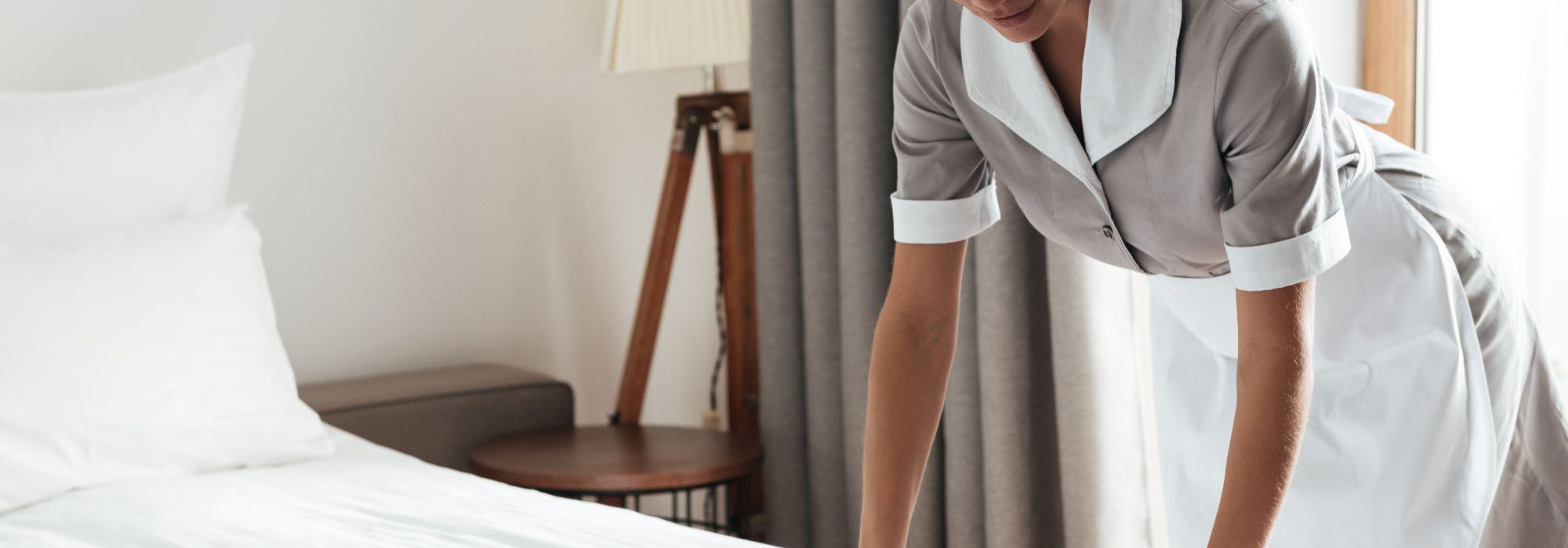 Maid setting up white bed sheet in hotel room Young hotel maid setting up white bed sheet in hotel room